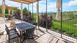 A covered outdoor patio with a table and chairs, overlooking a vineyard. - Scenic Apartment in Ascoli Piceno with Hot Tub (Ripatransone)