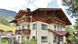 A two-story chalet with wooden balconies, a covered porch, and a mountain backdrop. - Apartment in Grossarl Near Ski Slopes (Grossarl)