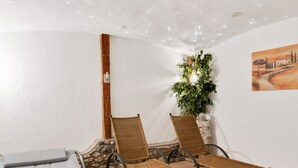 A room with two wicker lounge chairs, a bed, a stone wall, a plant, and a painting on the wall. - Apartment in Grossarl Near Ski Slopes (Grossarl)