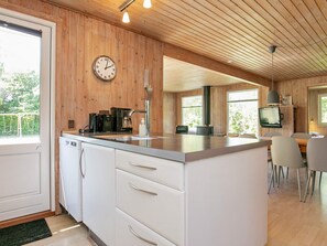 A modern kitchen with a built-in island, wooden walls, a clock, and a dining area with chairs.