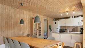 A wooden interior with a dining table, chairs, a kitchen area, and pendant lights.