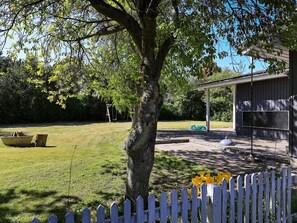 A tree-lined yard with a swing set, a boat, and a white picket fence.
