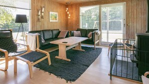 A cozy cabin interior with a wooden ceiling, a green sofa, a wooden table, and a fireplace.