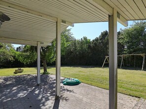 A covered outdoor area with a paved patio, a swing set, and a lawn.