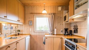 Een kleine keuken met houten kastjes, een inbouwoven, een magnetron en een koffiezetapparaat.