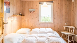 Een houten kamer met een bed, een stoel, een raam en een plank met decoratieve objecten.