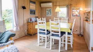 Een gezellig houten huisje met een eethoek, inclusief een tafel en stoelen, een kleine kitchenette en een raam met gordijnen.