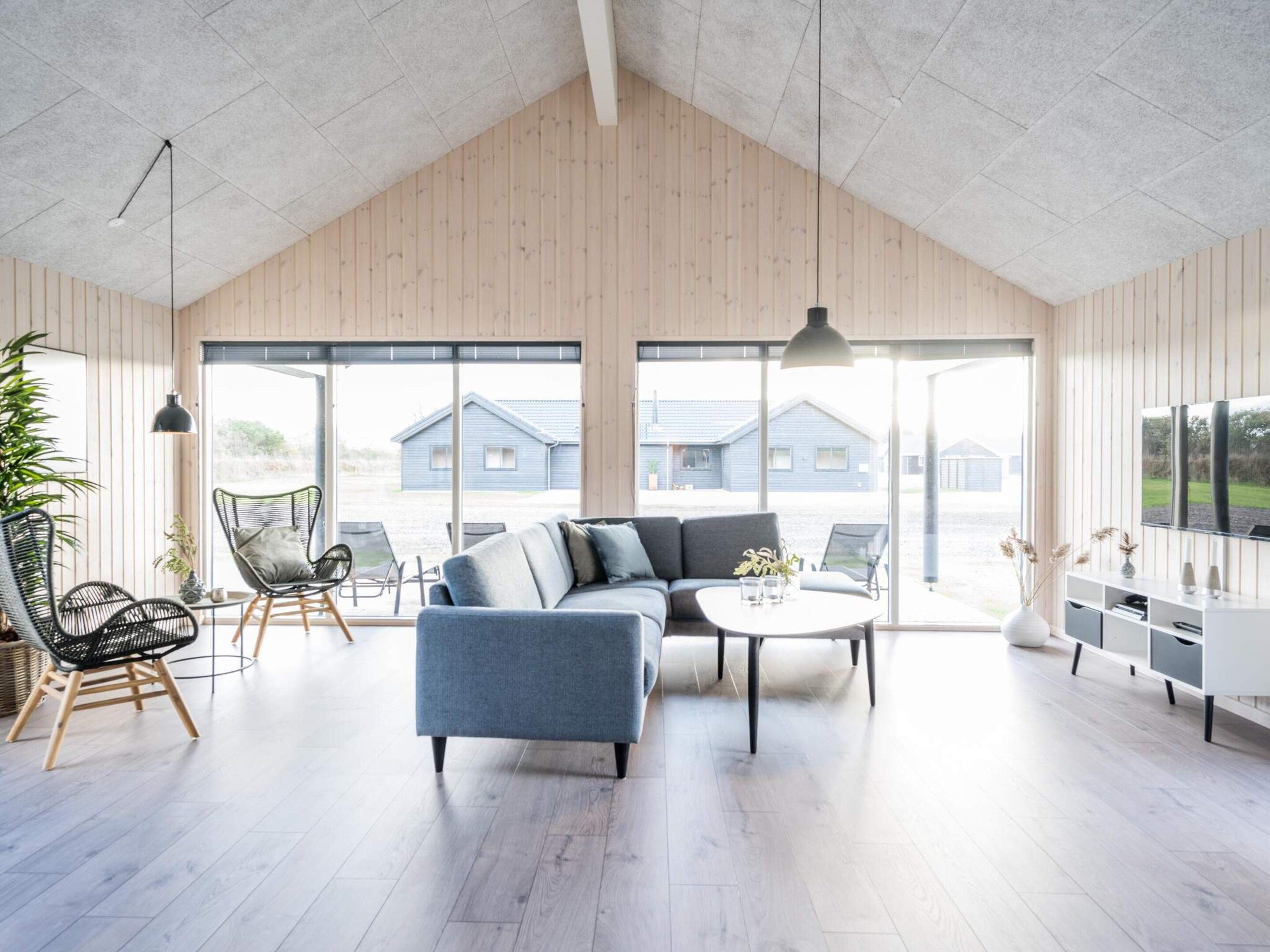 A spacious living room with a high ceiling, large windows, a sectional sofa, and a television.