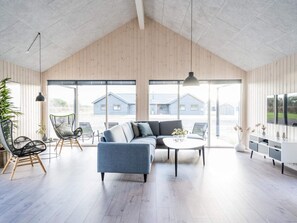 Amplia sala de estar con techo alto, ventanas grandes, sofá modular y televisor.