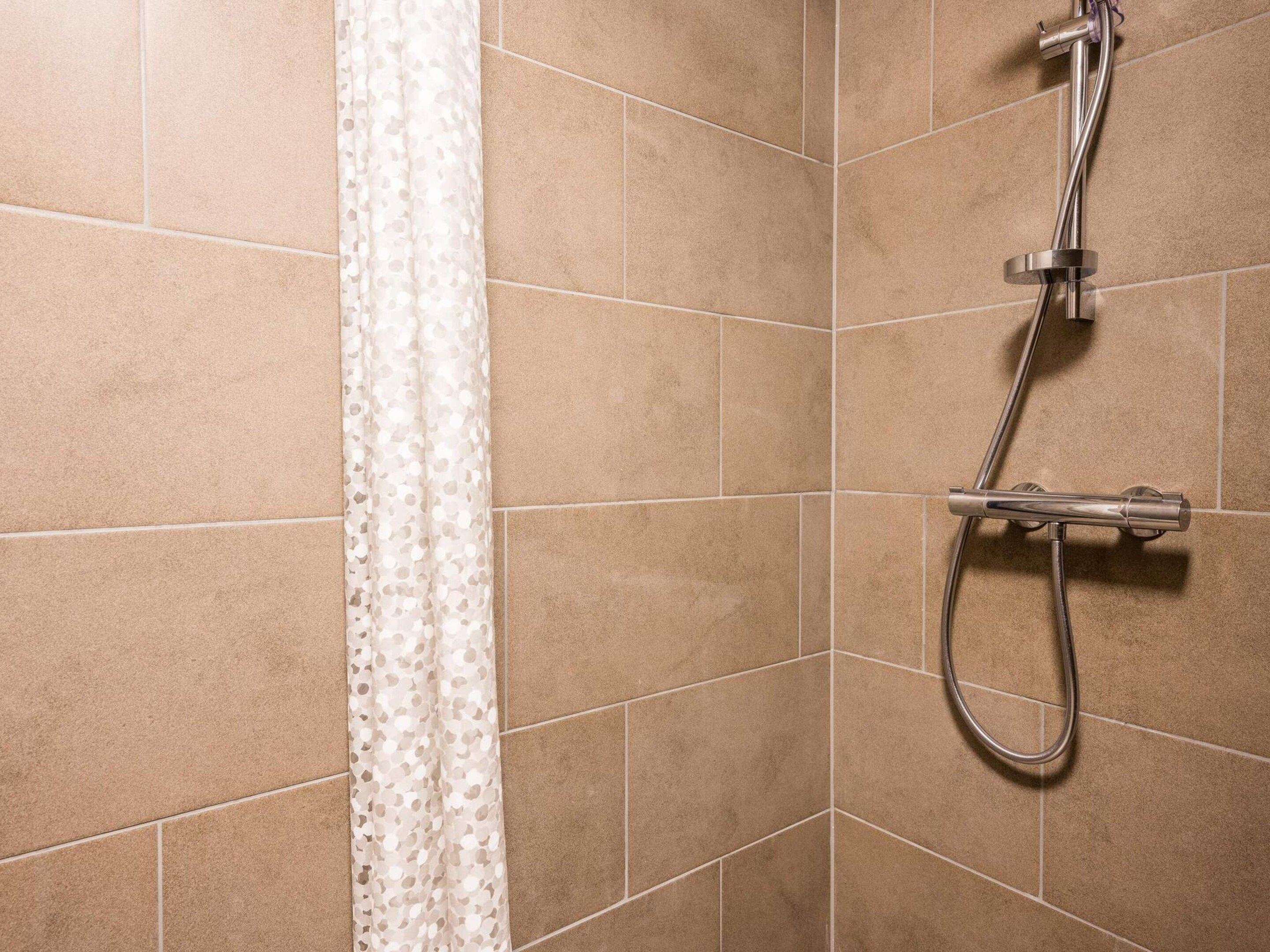A shower with a handheld showerhead and a curtain.