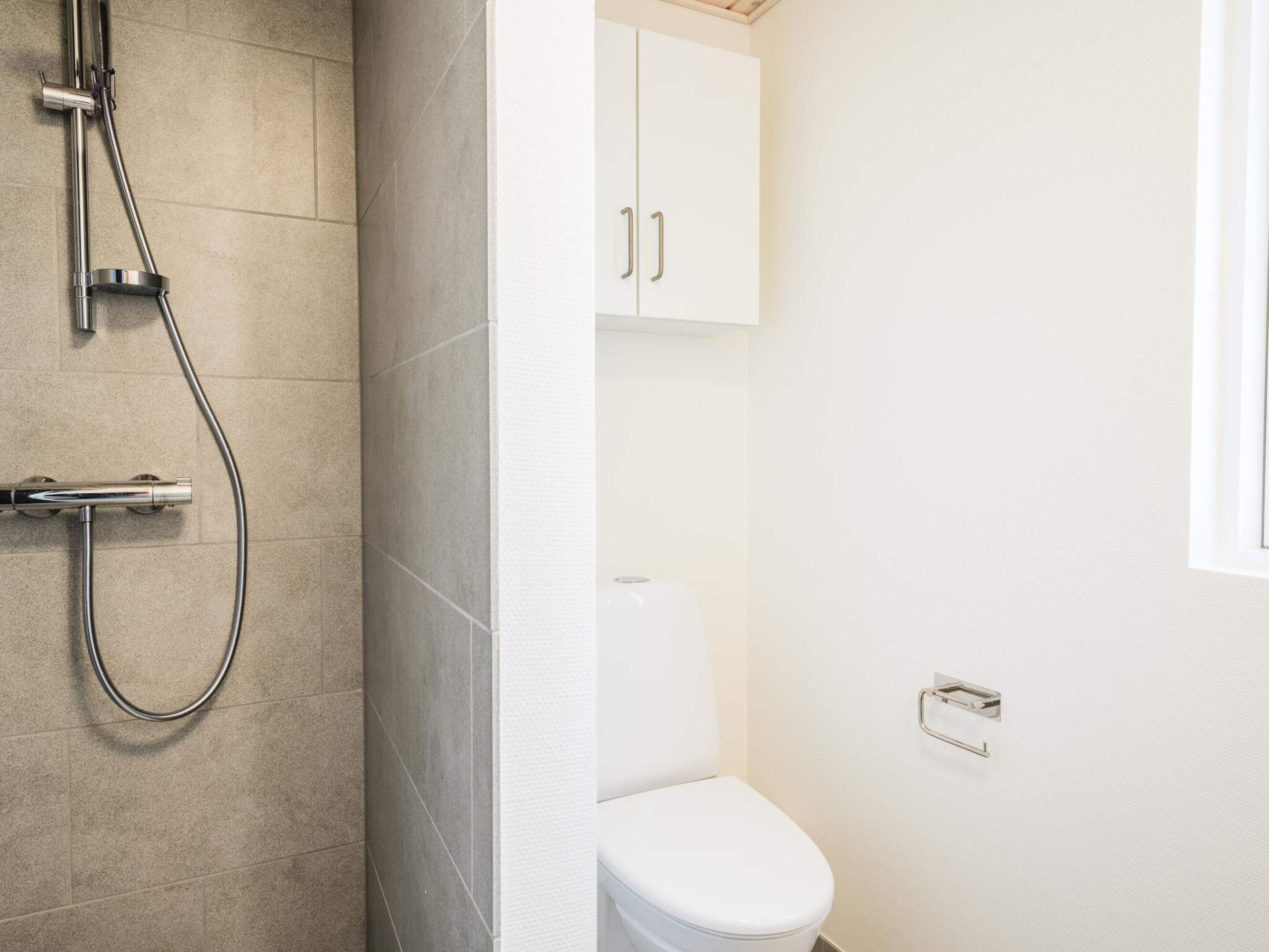 Un baño con ducha, inodoro y un armario.