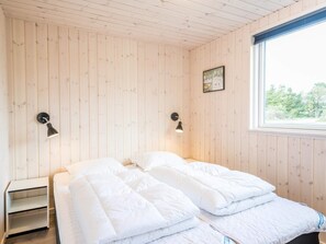 A room with wooden walls, a bed with white bedding, two wall-mounted lamps, and a window with a view of trees. - 5 Star Holiday Home in Norre Nebel (Norre Nebel)