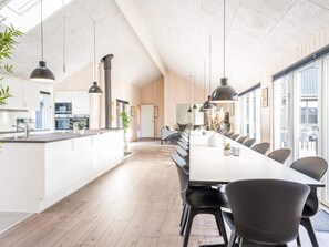 A modern kitchen with a central island, wooden flooring, pendant lighting, and a view to the outside. - 5 Star Holiday Home in Norre Nebel (Norre Nebel)