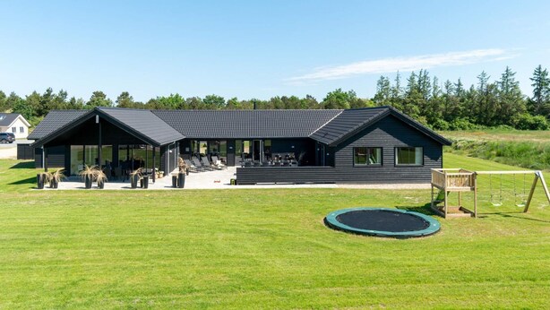 A modern building with a covered patio area, a lawn, and a trampoline. - 5 Star Holiday Home in Norre Nebel (Norre Nebel)