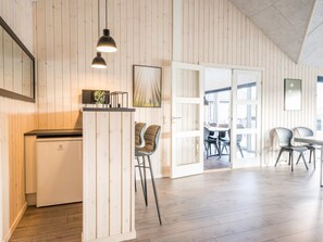 A modern kitchen with a built-in refrigerator, wooden panel walls, and a dining area with chairs and a table. - 5 Star Holiday Home in Norre Nebel (Norre Nebel)