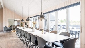 A long dining table with chairs, pendant lights, and a view of the outdoors. - 5 Star Holiday Home in Norre Nebel (Norre Nebel)