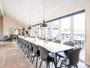 Una larga mesa de comedor con sillas, lámparas colgantes y vistas al exterior.