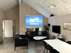 A modern conference room with a large screen, black leather sofas, a white table, and a flat-screen TV.