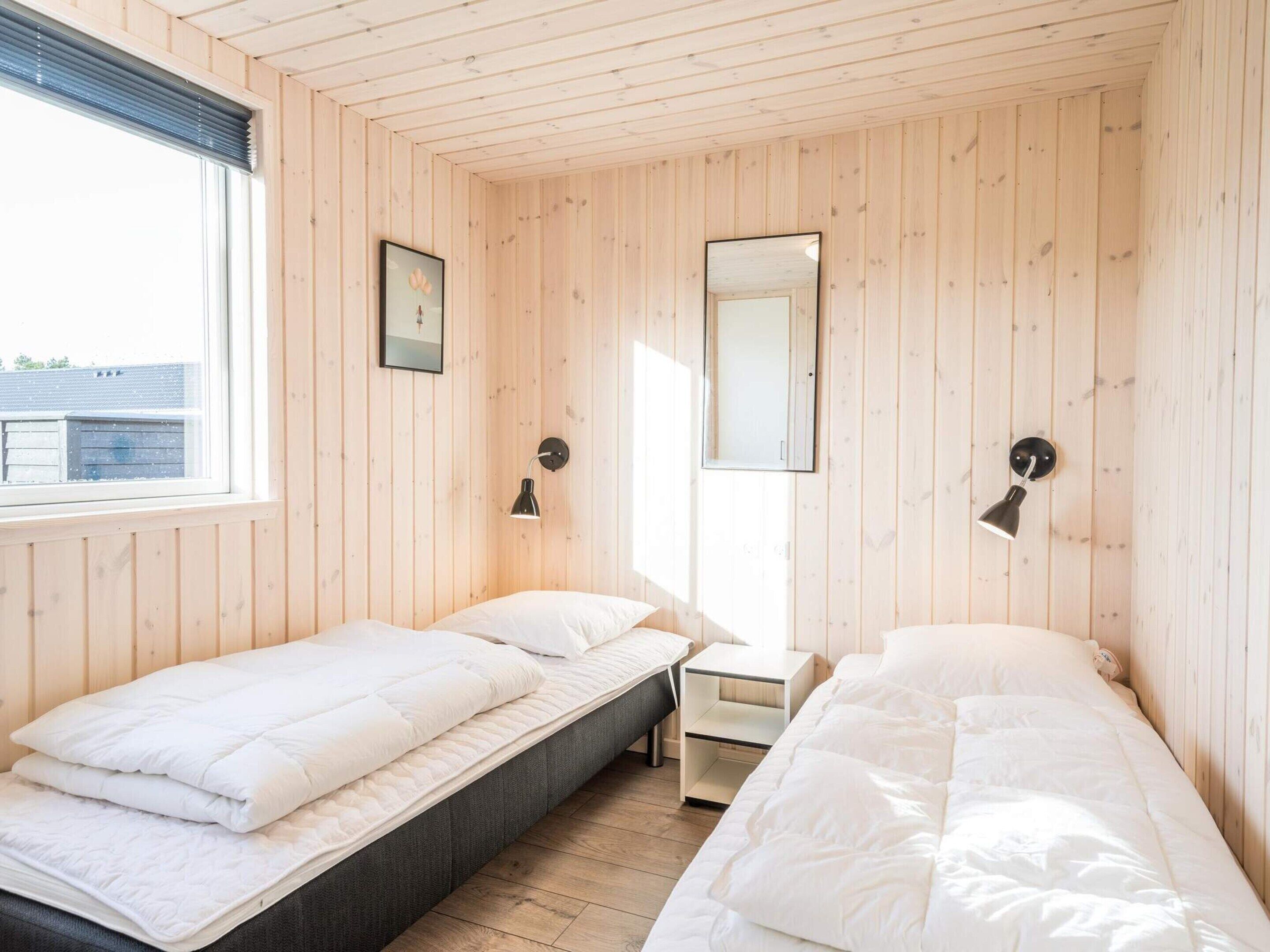 A room with two beds, a small table, a mirror, and two wall-mounted lamps.