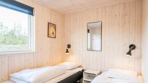 A room with two beds, a small table, a window, and a mirror. - 5 Star Holiday Home in Norre Nebel (Norre Nebel)