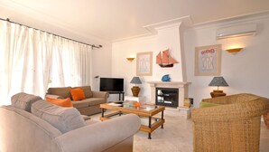A living room with a sofa, armchair, and a fireplace. There is a television and a lamp on a side table. - Beautiful Villa Located Less Than Five Minutes Walk From the Old Village (Loulé)