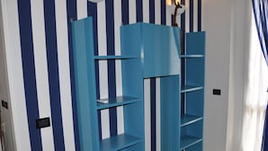 Une pièce avec un mur rayé bleu et blanc, une étagère bleue et une fenêtre avec des rideaux.