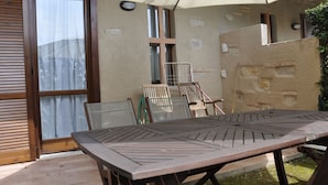 Un espace patio avec une table et des chaises en bois, un coin salon abrité et une vue sur un bâtiment à la façade en pierre.