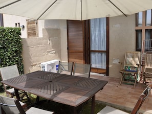 An outdoor patio area with a wooden table and chairs, a white umbrella, and a small air conditioning unit. - Poolside Stay in Lazise (Lazise)