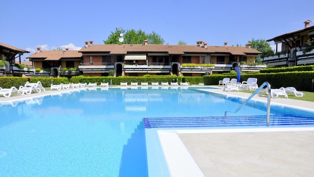 Une piscine avec des chaises longues et, au fond, un bâtiment doté de nombreux balcons.