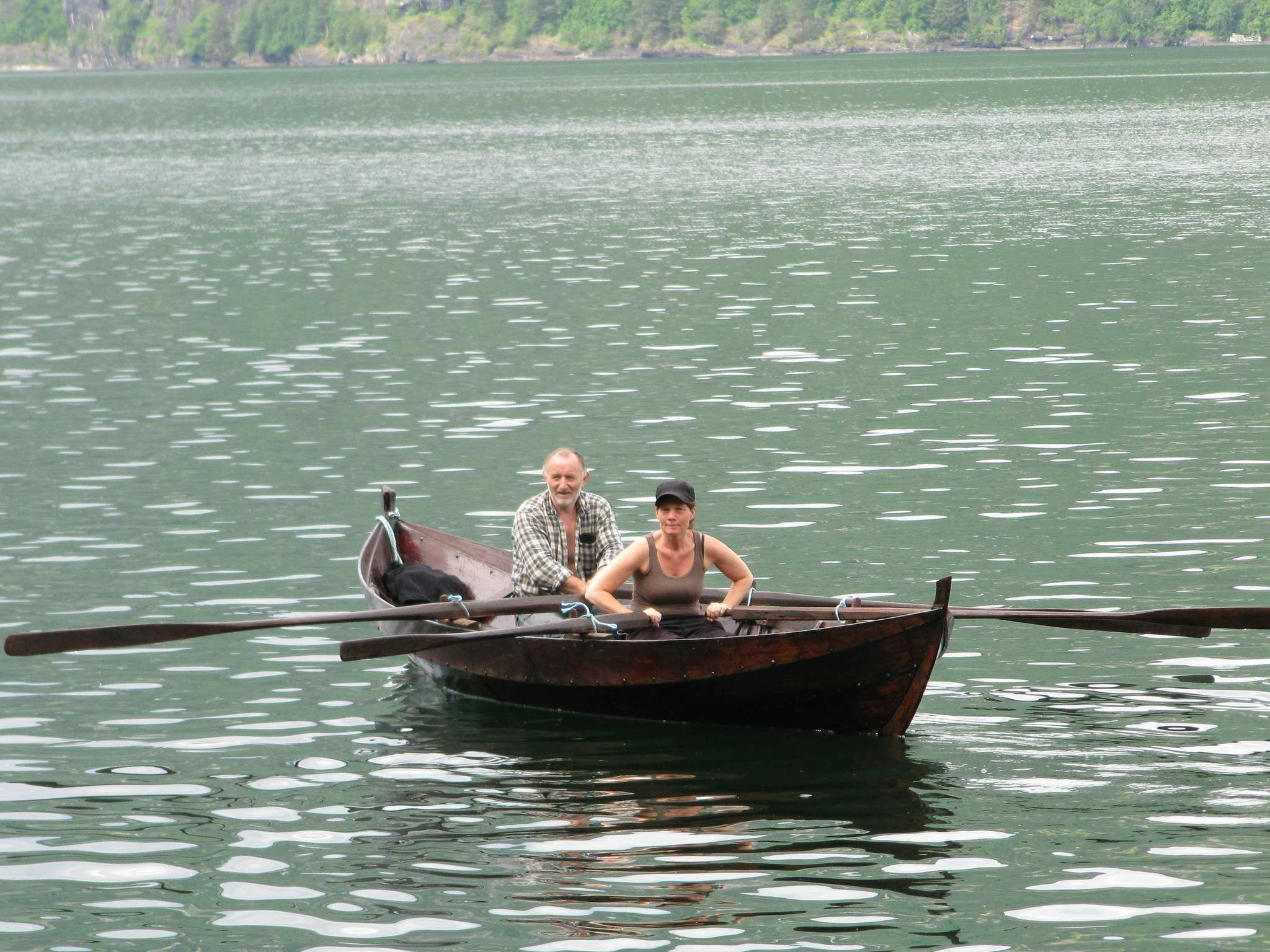 Ein hölzernes Boot mit zwei Ruderern auf einem ruhigen See.
