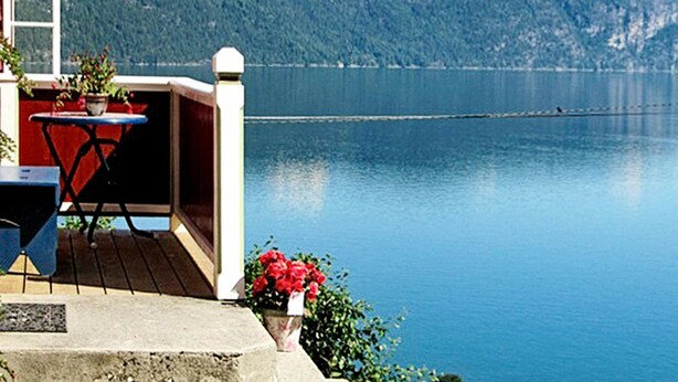 A balcony with a table and chairs, overlooking a calm lake and forested hills. - 4 Person Holiday Home in Utvik (Stryn)