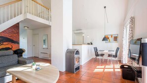A spacious living area with a high ceiling, a fireplace, a dining table with chairs, and a TV mounted on the wall. - 4 Star Holiday Home in Blavand (Blavand)