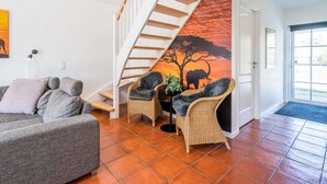 A living room with a sofa, two wicker chairs, a staircase, and a sunset mural on the wall. - 4 Star Holiday Home in Blavand (Blavand)