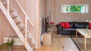 A wooden interior with a staircase, a black leather sofa, a wooden coffee table, and a window with a view. - Holiday Home in Sydals (Sydals)