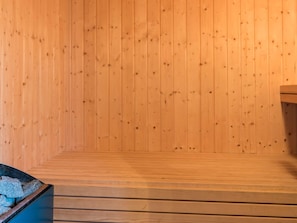 Un sauna en bois, doté de bancs et d’un récipient en pierre.