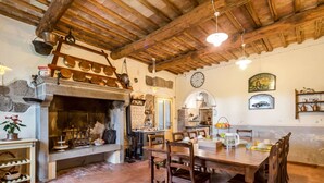 A rustic dining area with a stone fireplace, wooden ceiling beams, and a tiled floor.