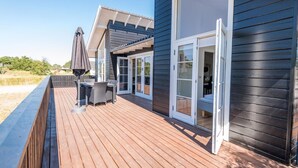 A wooden deck with a table and chairs, a sliding glass door, and a beach view.