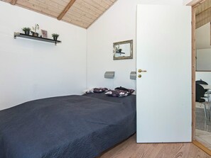 A bedroom with a bed, a door, a mirror, and a shelf with plants.