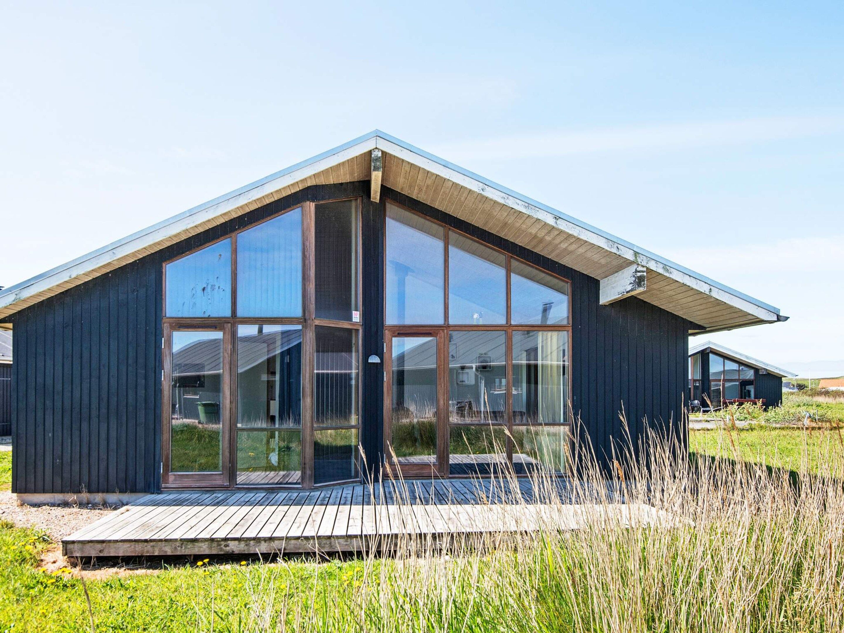 A modern building with large windows, a wooden deck, and a grassy field in the background.