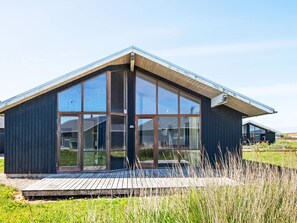 A modern building with large windows, a wooden deck, and a grassy field in the background. - Holiday Home in Ulfborg (Ulfborg)