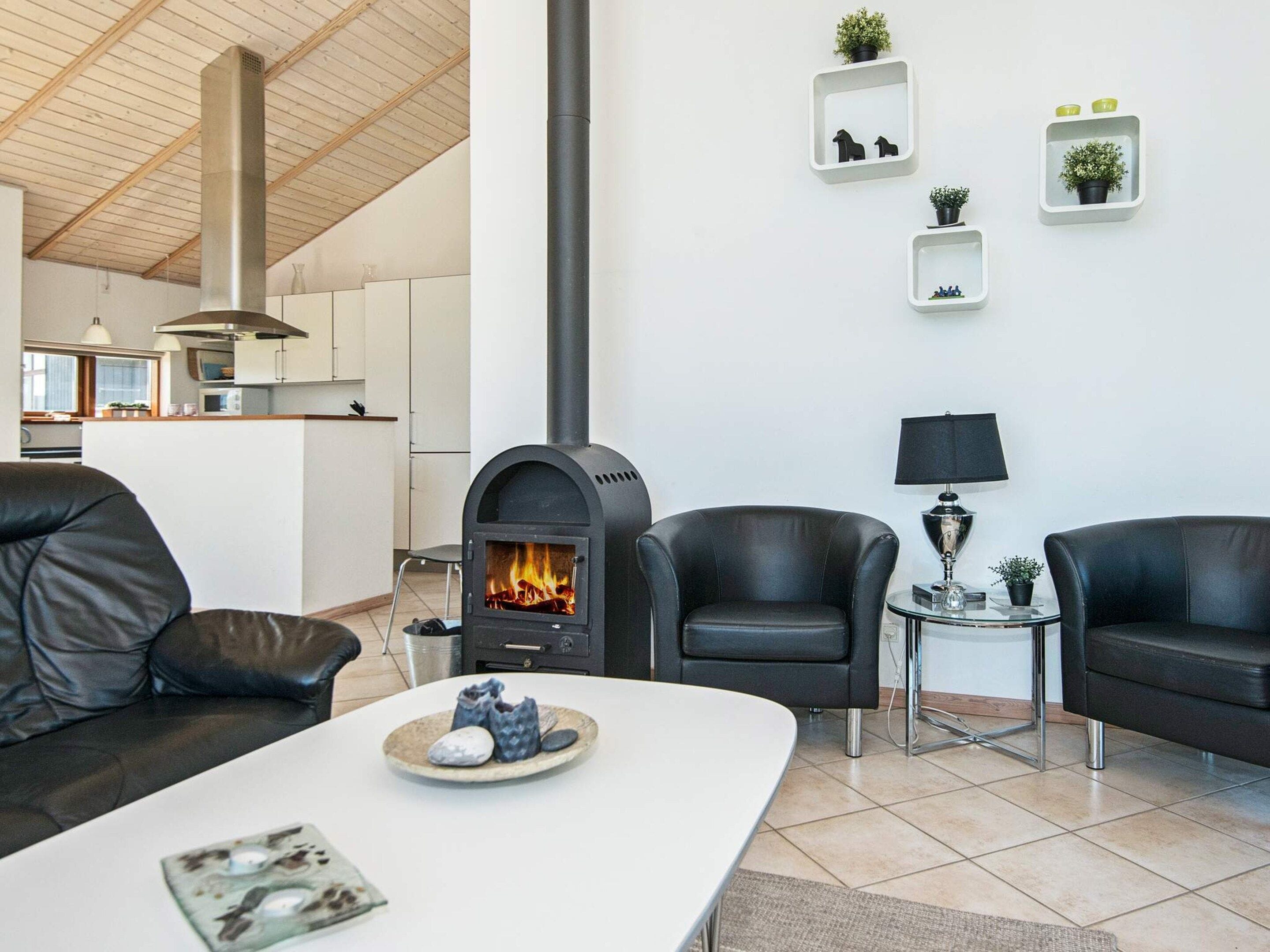 Una sala de estar moderna con chimenea, sofás de cuero, una mesa de comedor y una cocina al fondo.