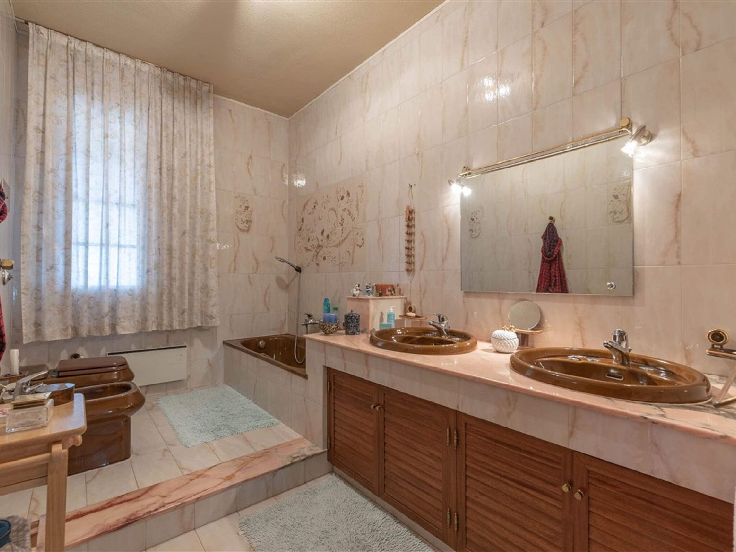 A bathroom with marble walls, a wooden vanity with two sinks, a bathtub, and a large mirror.