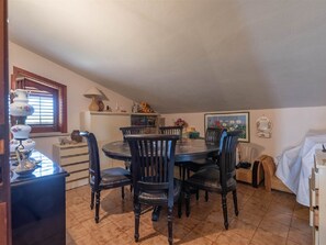 A dining area with a round table and six chairs, a window with blinds, a lamp, and a painting on the wall. - Marvellous Holiday Home near Palermo with Pool & Garden (Misilmeri)
