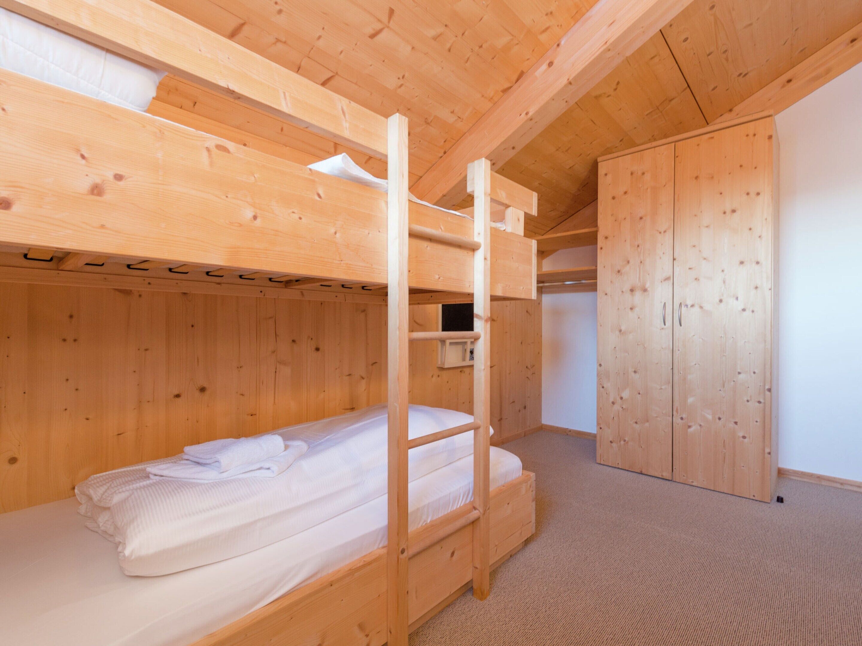 Une chambre avec des lits superposés, des murs en bois et un sol recouvert de moquette.