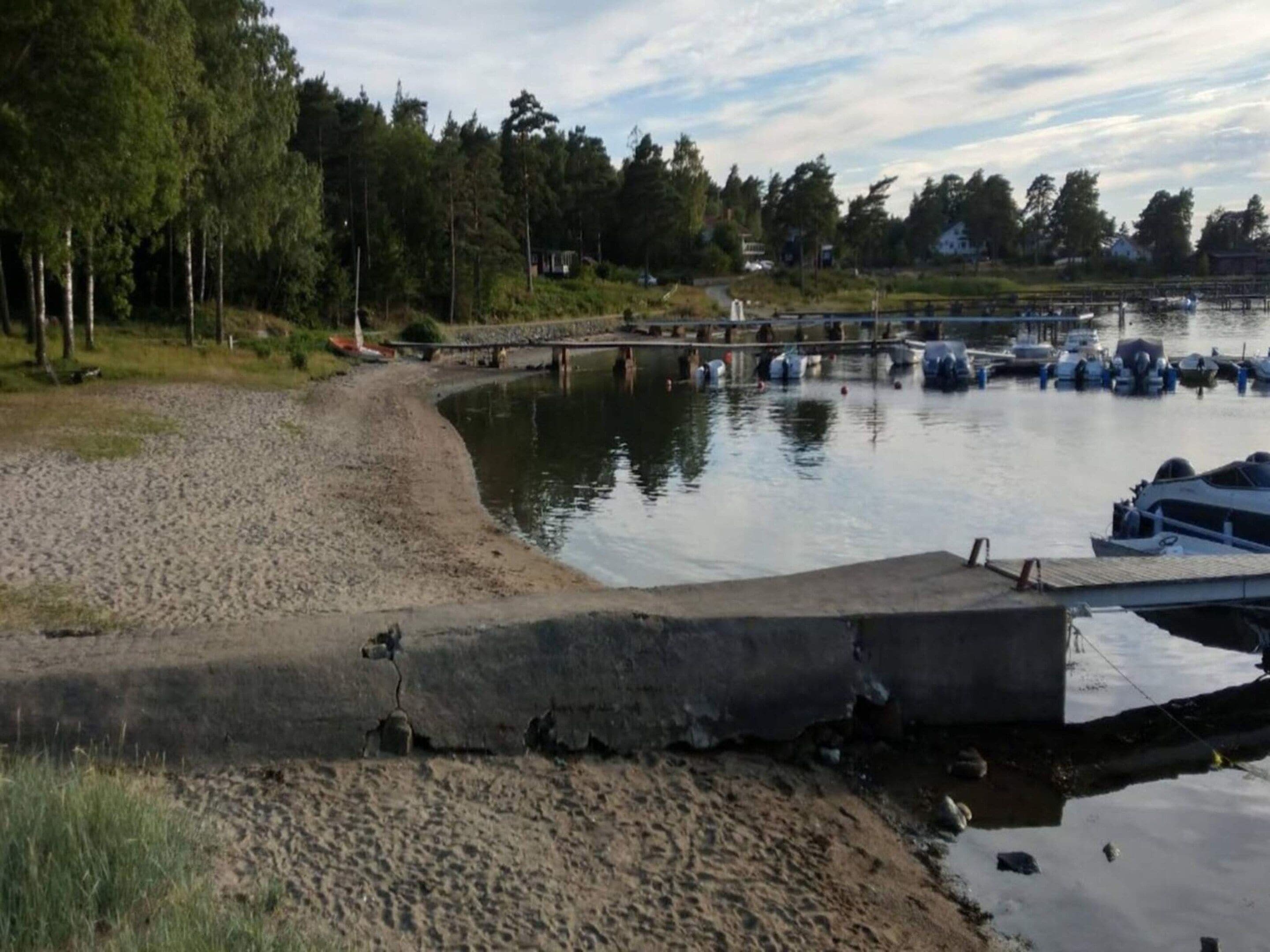 A lakeside area with boats docked, a concrete walkway, and a forested background.