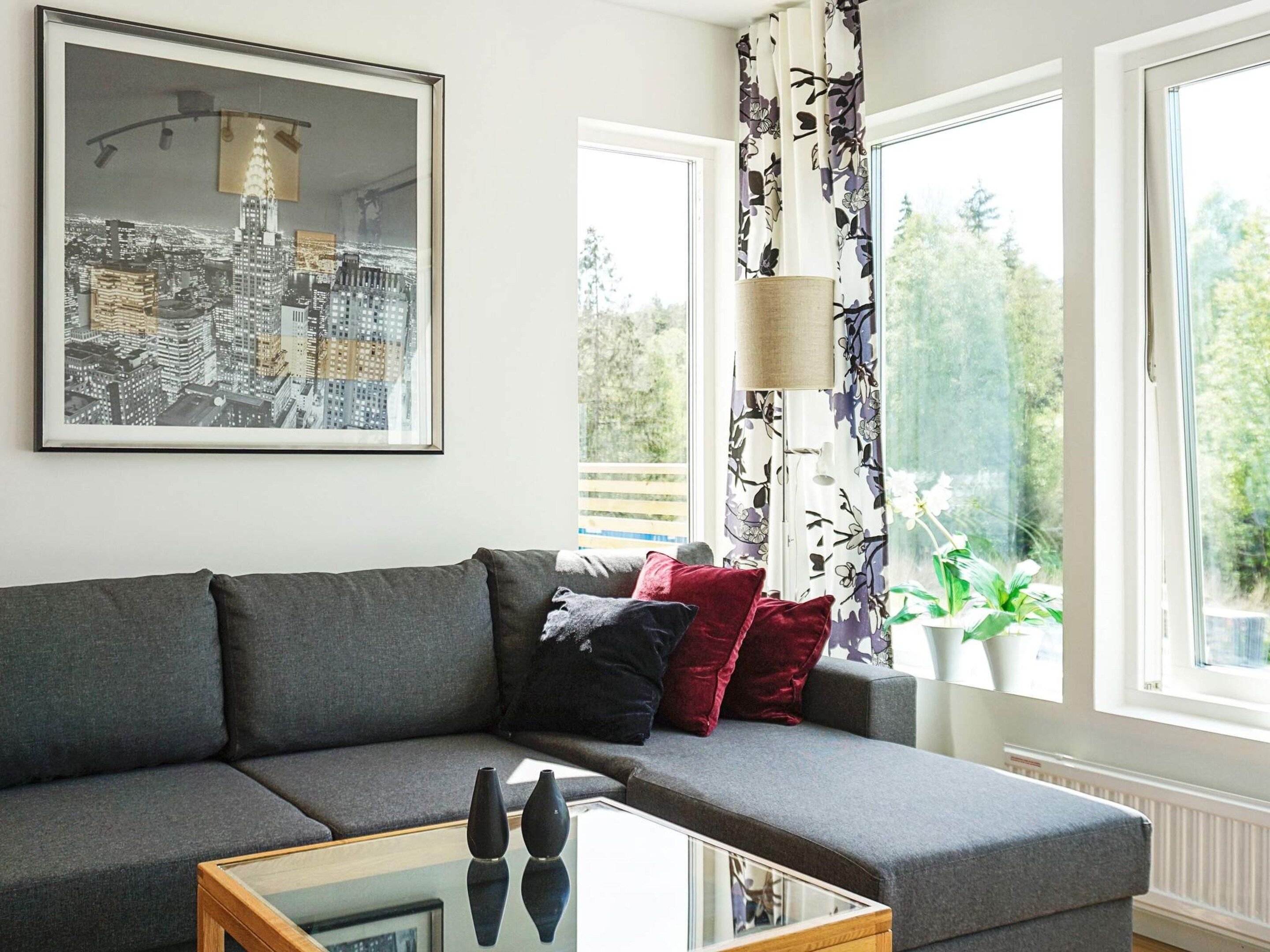 A modern living room with a grey sofa, a glass coffee table, and a framed cityscape picture on the wall.