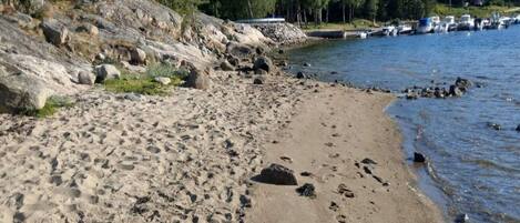 A sandy beach with visible footprints, a rocky shoreline, and boats in the water.