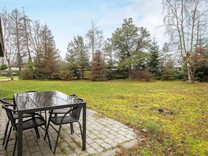 An outdoor patio with a table and chairs, surrounded by a grassy area and trees. - 6 Person Holiday Home in Vaeggerlose (Vaeggerlose)