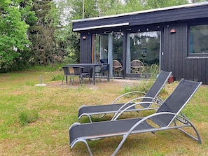 A modern outdoor seating area with lounge chairs and a table, surrounded by a wooden building with large windows. - 6 Person Holiday Home in Vaeggerlose (Vaeggerlose)