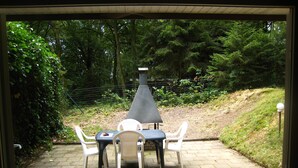 Une terrasse extérieure avec une table et des chaises, entourée d’un jardin et d’une clôture.